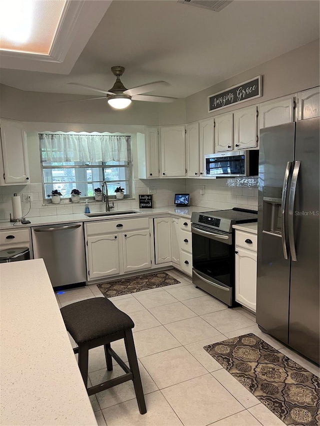 kitchen featuring light tile patterned flooring, sink, white cabinetry, appliances with stainless steel finishes, and decorative backsplash