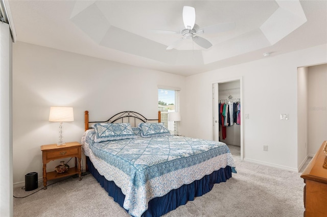 carpeted bedroom featuring ceiling fan, a closet, a raised ceiling, and a walk in closet