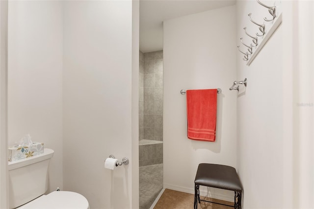 bathroom with tile patterned flooring, a tile shower, and toilet