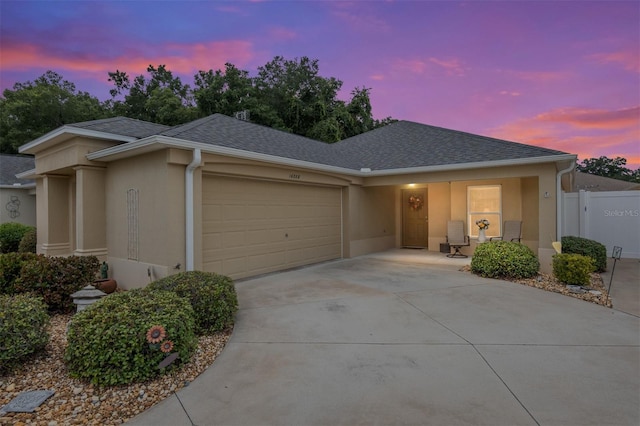 view of front of house featuring stucco siding, a garage, roof with shingles, and fence