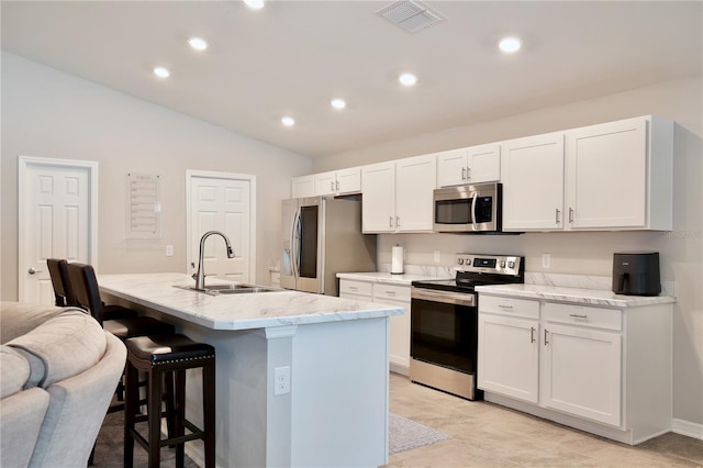 kitchen with appliances with stainless steel finishes, white cabinets, lofted ceiling, a kitchen island with sink, and sink