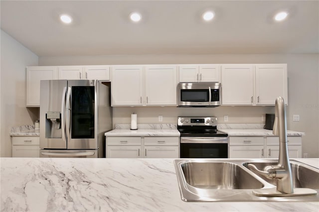 kitchen with light stone countertops, white cabinets, appliances with stainless steel finishes, and sink