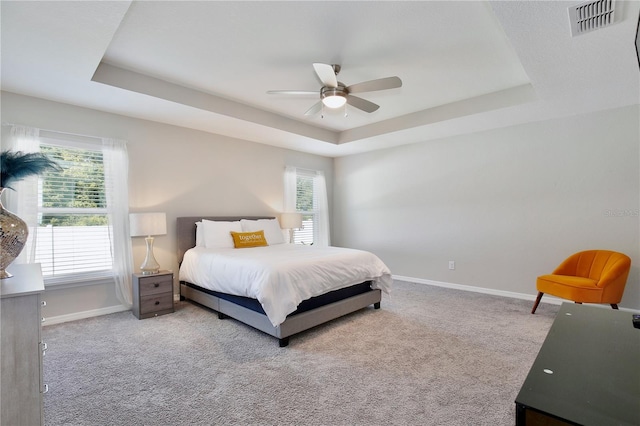 carpeted bedroom with a raised ceiling and ceiling fan