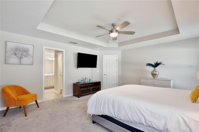 bedroom with a raised ceiling, light carpet, ceiling fan, and ensuite bathroom