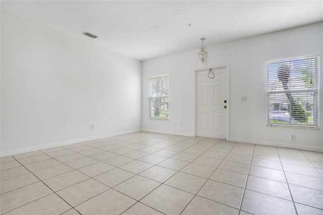 tiled empty room with plenty of natural light and an inviting chandelier