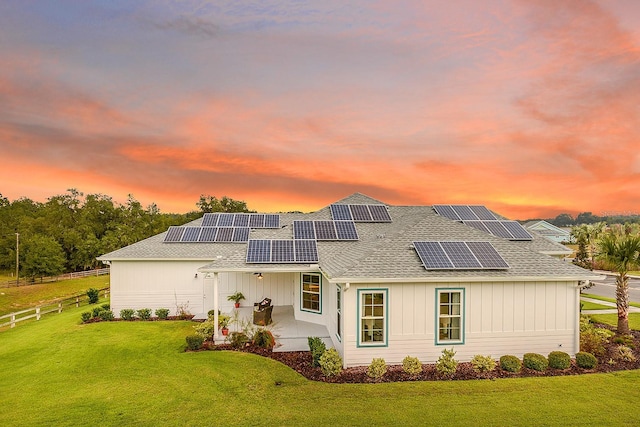 back house at dusk with a lawn and solar panels