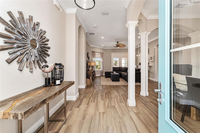 interior space featuring light wood-type flooring, crown molding, a textured ceiling, ceiling fan, and ornate columns