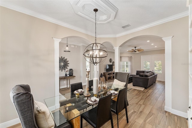 dining room with light wood-type flooring, ceiling fan with notable chandelier, crown molding, and ornate columns