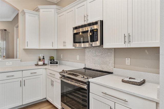 kitchen featuring appliances with stainless steel finishes, light stone countertops, light hardwood / wood-style floors, white cabinetry, and ornamental molding