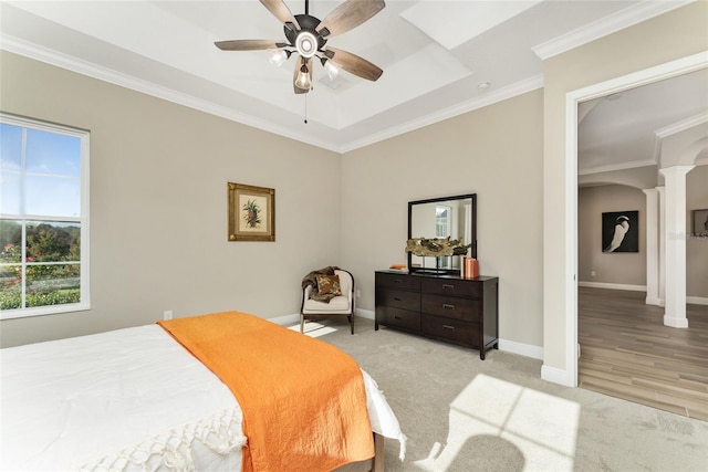 bedroom featuring a tray ceiling, decorative columns, light hardwood / wood-style floors, ornamental molding, and ceiling fan