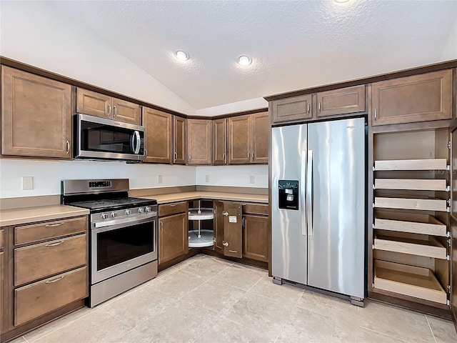 kitchen featuring appliances with stainless steel finishes, vaulted ceiling, light tile patterned floors, and a textured ceiling