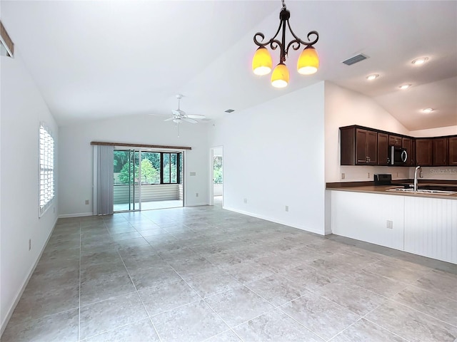 unfurnished living room with ceiling fan with notable chandelier, light tile patterned floors, sink, and vaulted ceiling