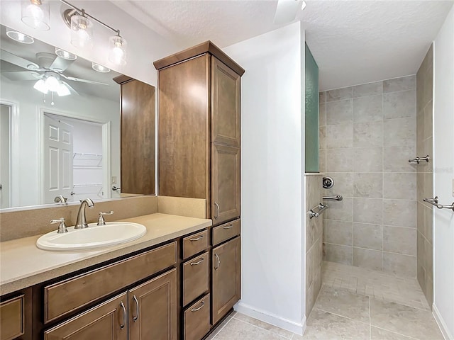 bathroom with tile patterned flooring, vanity, a textured ceiling, a tile shower, and ceiling fan