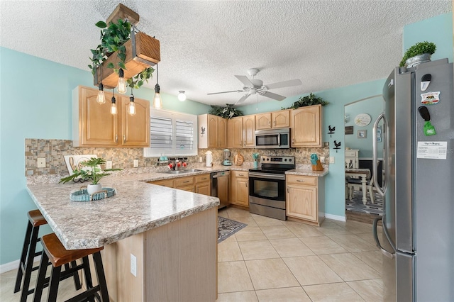 kitchen with a textured ceiling, appliances with stainless steel finishes, a breakfast bar, kitchen peninsula, and ceiling fan