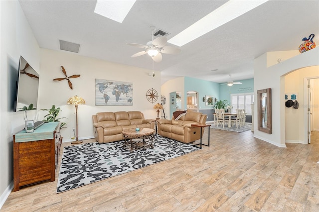 living room featuring light wood-type flooring, a textured ceiling, a skylight, and ceiling fan