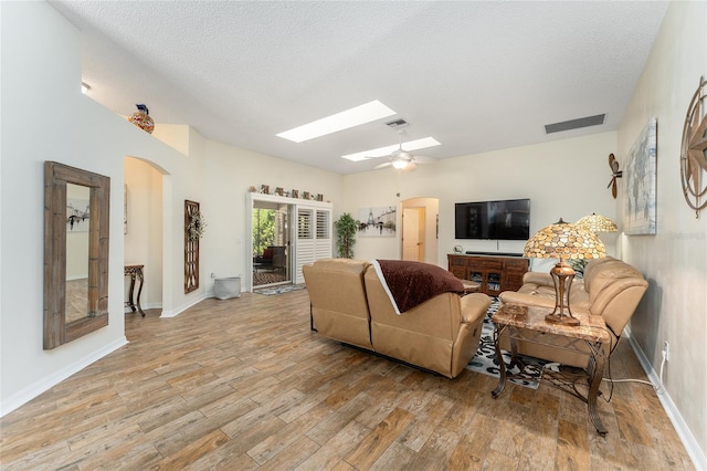 living room featuring a textured ceiling, a skylight, light hardwood / wood-style flooring, and ceiling fan