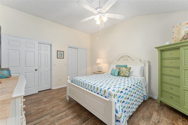 bedroom with ceiling fan, dark hardwood / wood-style floors, multiple closets, and vaulted ceiling