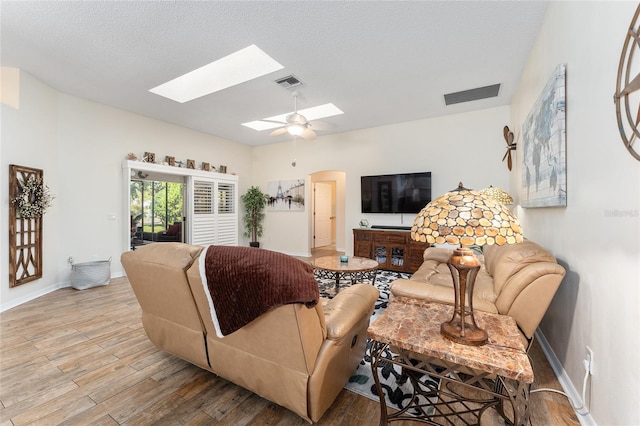 living room featuring light wood-type flooring, a skylight, ceiling fan, and a textured ceiling