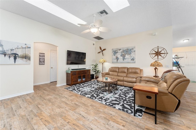 living room featuring light wood-type flooring, a skylight, ceiling fan, and a textured ceiling