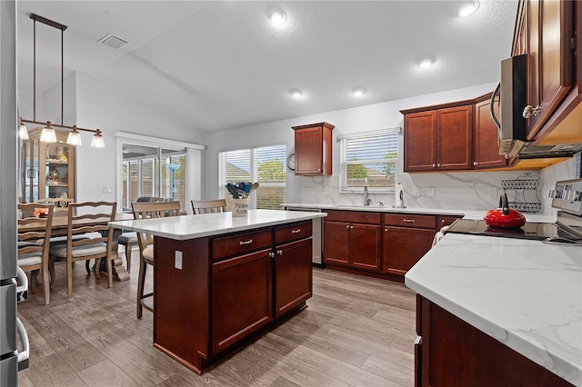 kitchen featuring pendant lighting, vaulted ceiling, appliances with stainless steel finishes, a breakfast bar, and light hardwood / wood-style floors