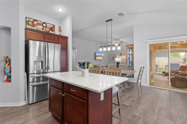 kitchen featuring pendant lighting, lofted ceiling, a kitchen island, stainless steel refrigerator with ice dispenser, and light wood-type flooring