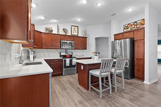 kitchen with stainless steel appliances, light wood-type flooring, lofted ceiling, a center island, and sink