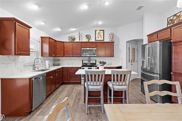 kitchen featuring appliances with stainless steel finishes, backsplash, light wood-type flooring, lofted ceiling, and sink