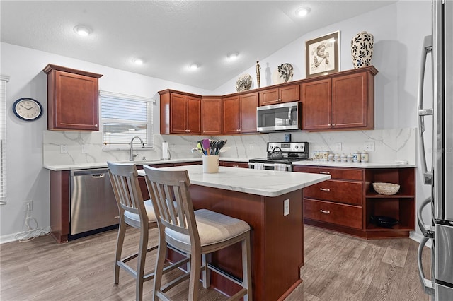 kitchen featuring appliances with stainless steel finishes, light hardwood / wood-style floors, backsplash, lofted ceiling, and a center island