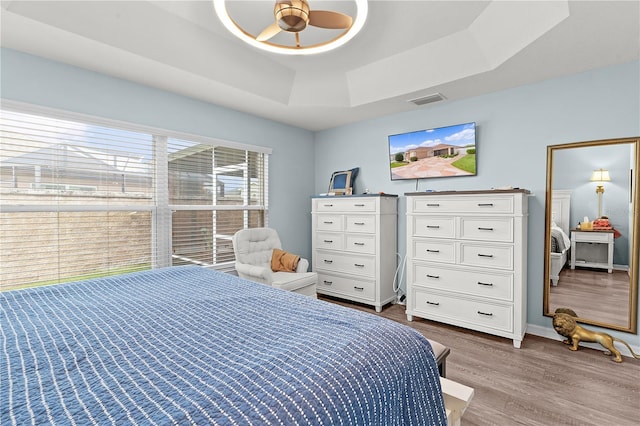 bedroom with wood-type flooring, a raised ceiling, and ceiling fan