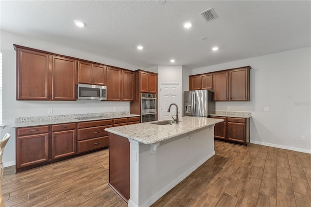 kitchen with an island with sink, dark wood-type flooring, stainless steel appliances, and sink