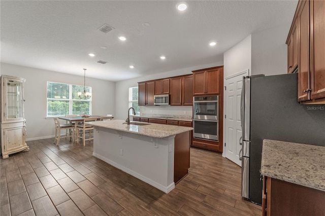 kitchen featuring decorative light fixtures, stainless steel appliances, an island with sink, light stone countertops, and dark hardwood / wood-style floors