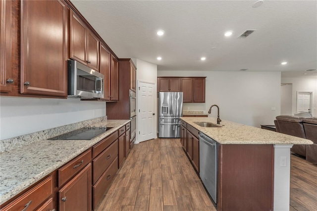 kitchen featuring dark hardwood / wood-style flooring, a center island with sink, stainless steel appliances, sink, and light stone counters