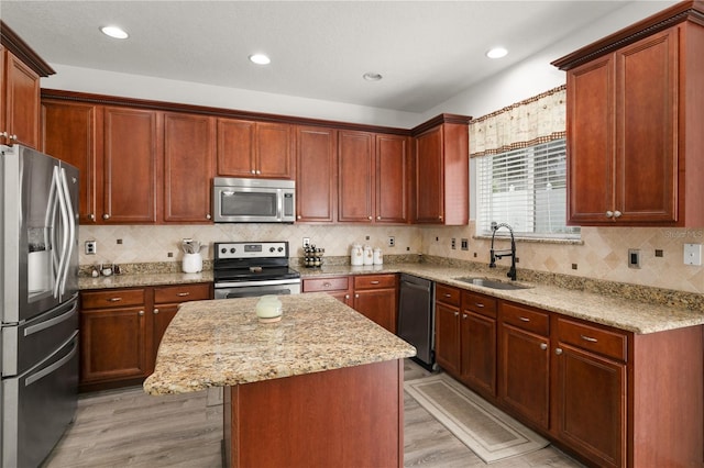 kitchen featuring a kitchen island, light stone countertops, appliances with stainless steel finishes, sink, and light wood-type flooring