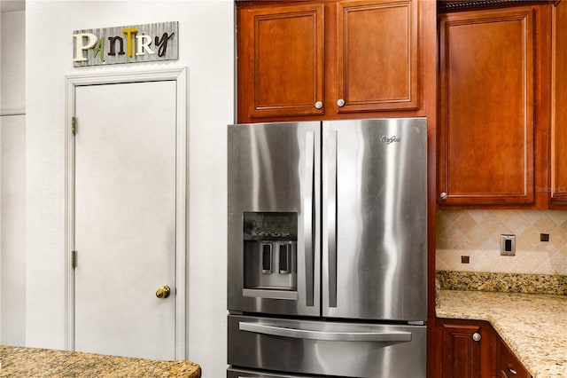 kitchen featuring backsplash, light stone counters, and stainless steel refrigerator with ice dispenser