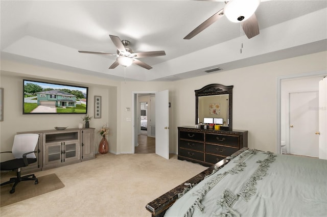 carpeted bedroom with a tray ceiling, ensuite bath, and ceiling fan