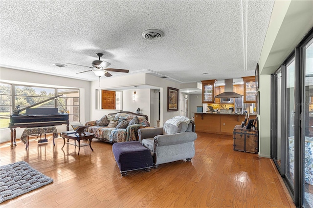 living room featuring ceiling fan, a textured ceiling, light hardwood / wood-style flooring, and crown molding