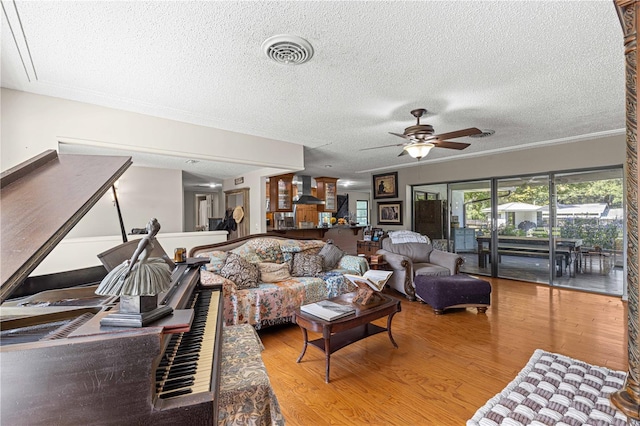 living room featuring a textured ceiling, wood-type flooring, ornamental molding, and ceiling fan