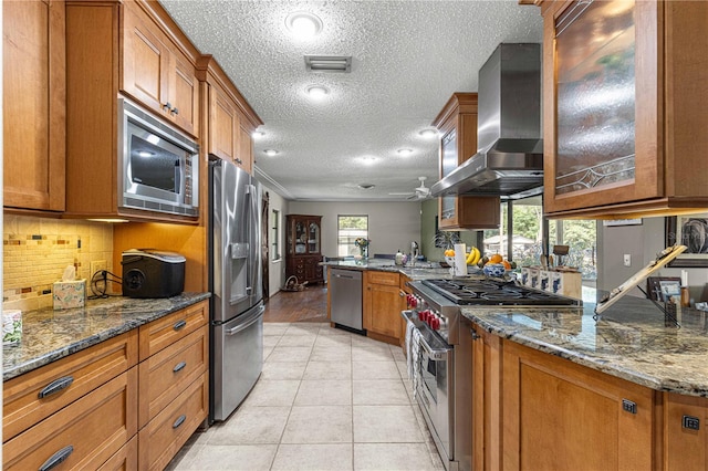 kitchen with wall chimney exhaust hood, stone countertops, light tile patterned floors, and stainless steel appliances