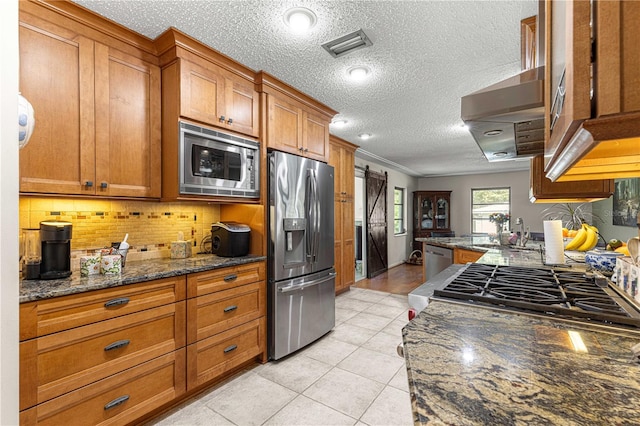 kitchen featuring light tile patterned floors, a textured ceiling, stainless steel appliances, dark stone counters, and decorative backsplash