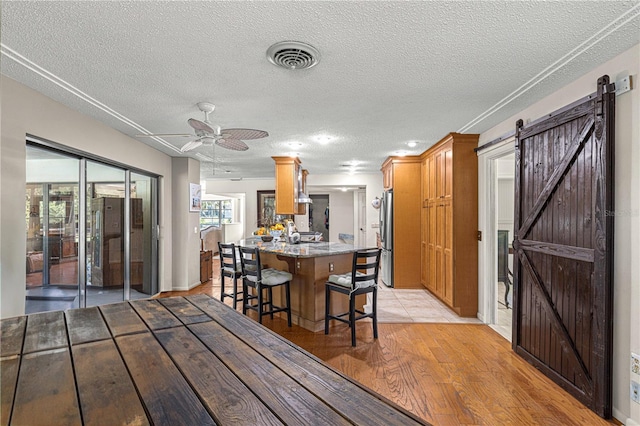 dining area with ceiling fan, a textured ceiling, light hardwood / wood-style flooring, and a barn door