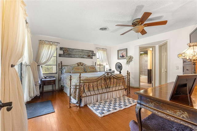 bedroom featuring ensuite bath, ceiling fan, hardwood / wood-style flooring, and a textured ceiling