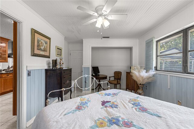 bedroom with ornamental molding, wood walls, ceiling fan, and light tile patterned flooring