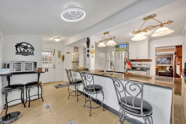 kitchen featuring dark stone countertops, white cabinetry, stainless steel appliances, a kitchen breakfast bar, and hanging light fixtures