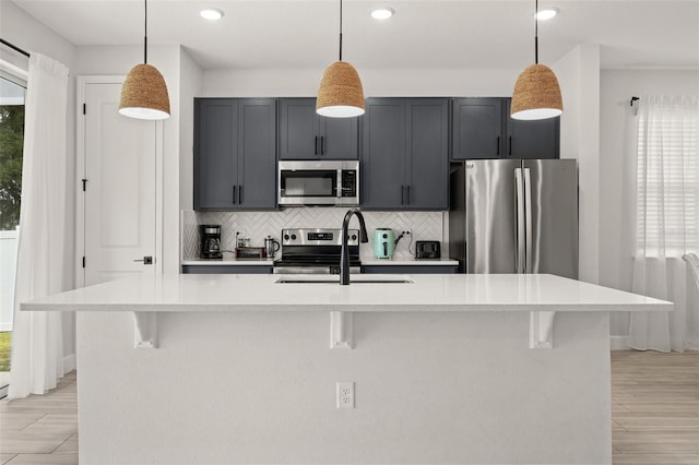 kitchen with decorative light fixtures, a center island with sink, and stainless steel appliances