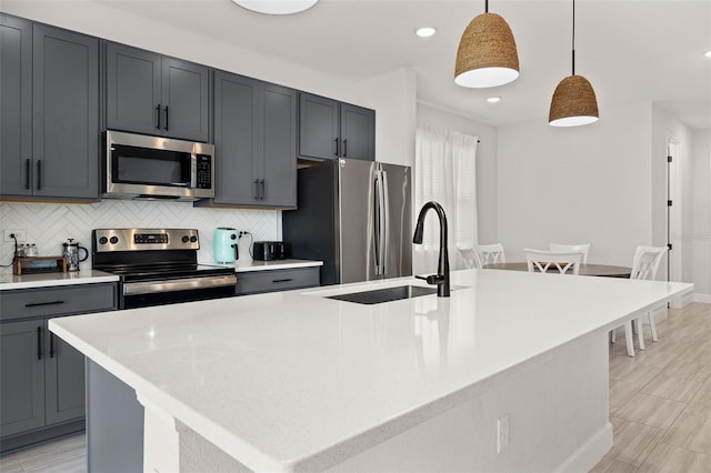 kitchen featuring a center island with sink, appliances with stainless steel finishes, hanging light fixtures, and sink