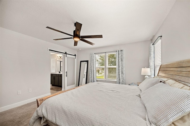 carpeted bedroom featuring a barn door, ensuite bath, and ceiling fan