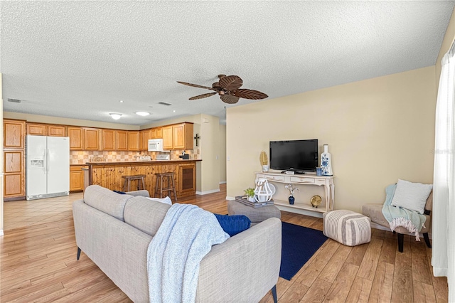 living room featuring a textured ceiling, light wood-type flooring, and ceiling fan