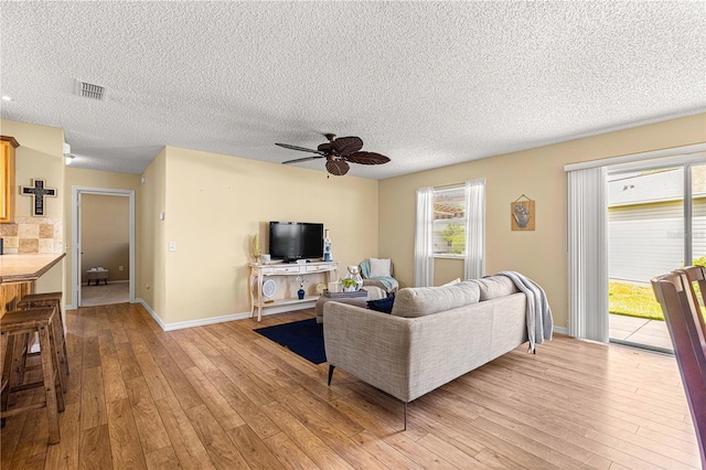 living room with a textured ceiling, light wood-type flooring, and ceiling fan