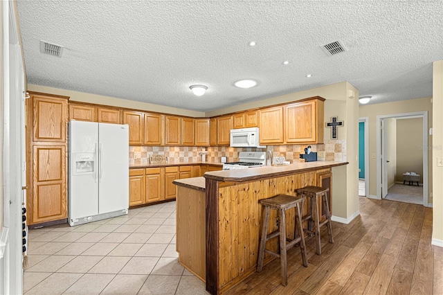 kitchen featuring white appliances, a kitchen bar, backsplash, kitchen peninsula, and light hardwood / wood-style floors