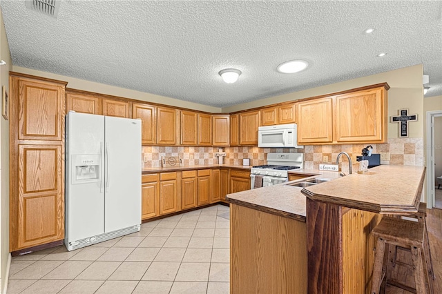 kitchen featuring kitchen peninsula, a textured ceiling, a breakfast bar, and white appliances